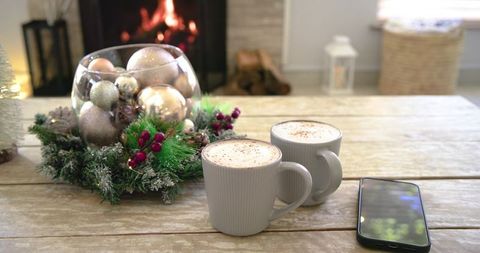 Steaming Latte Cups on Rustic Wood Table with Festive Wreath and Cozy Fireplace