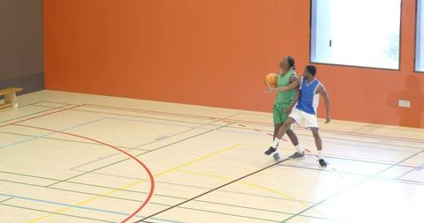 Diverse male teammates competing 1-on-1 drill driving for layup and stealing ball in gym