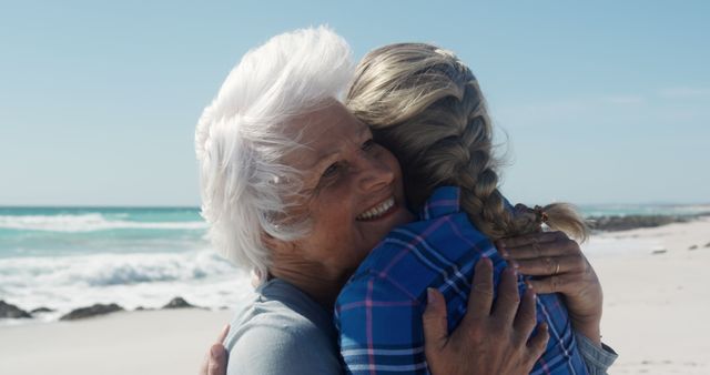 An elderly woman is happily embracing her adult daughter on a beautiful seaside. This image can be used to depict family love, togetherness, and the special bonds between generations. It is ideal for topics related to family relationships, aging, happiness, and enjoying time outdoors. This could also be used in advertising for family-oriented services or products, retirement plans, or health and wellness promotions.