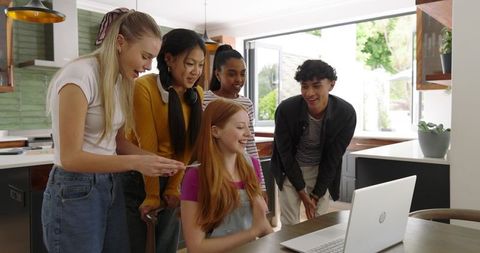 Teens Gathering Around Laptop Sharing Laughter, Smartphone and Headphones in Modern Kitchen