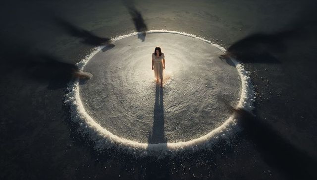 Solitary woman standing inside glowing salt circle on dark salt flat, dramatic shadow