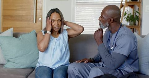 Home care consultation showing clinician assessing mature patient holding head in pain