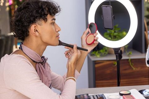 Male makeup influencer applying blush in ring-light studio setup