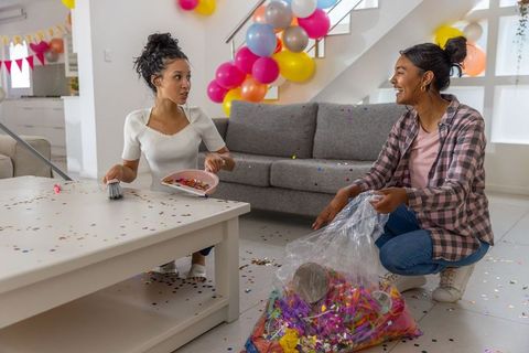 Mother and teen daughter cleaning confetti and sweeping together after colorful party
