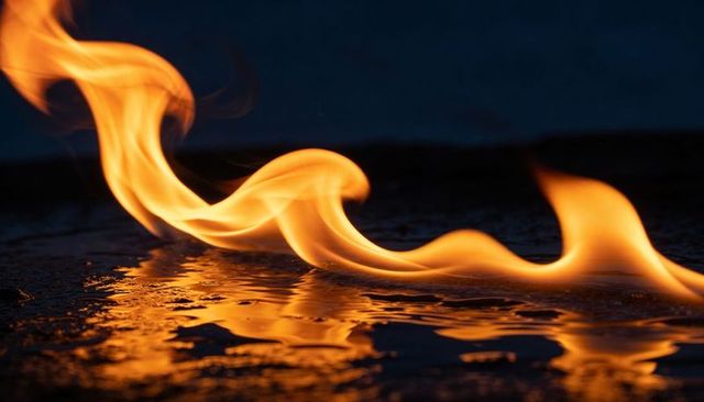 Dancing flame creating glowing ribbon reflection on wet pavement at night