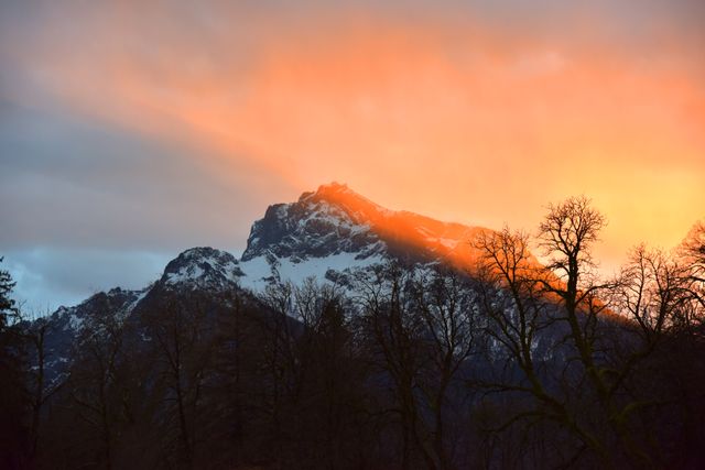 This picturesque scene captures the breathtaking view of a snow-capped mountain during a vibrant sunset, with dramatic orange hues lighting up the sky. Ideal for nature and travel blogs, outdoor adventure promotions, or inspirational posters, this image evokes a sense of tranquility and grandeur.