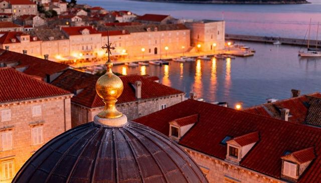 Golden finial over historic adriatic harbor at twilight, rooftop dome and marina view
