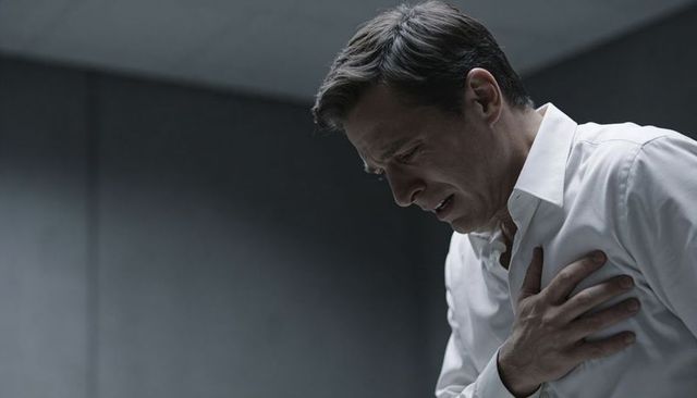 Middle-aged man clutching chest, experiencing heart attack symptom in desaturated room