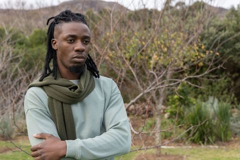 Brooding african american man standing arms crossed wearing olive scarf in overcast park
