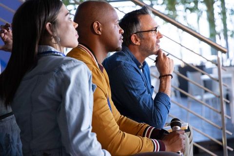 Diverse panelists listening during conference discussion holding microphone and notebook