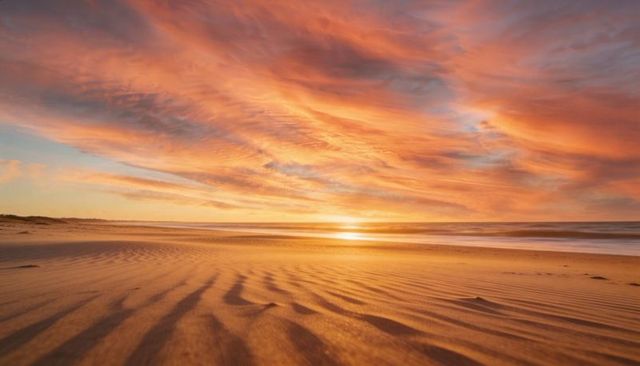 Golden sunset over rippling beach sand casting warm reflections across dramatic cloudscape
