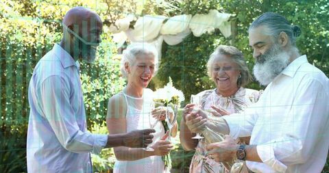 Mature friends celebrating in sunlit garden pouring champagne and toasting with stemware