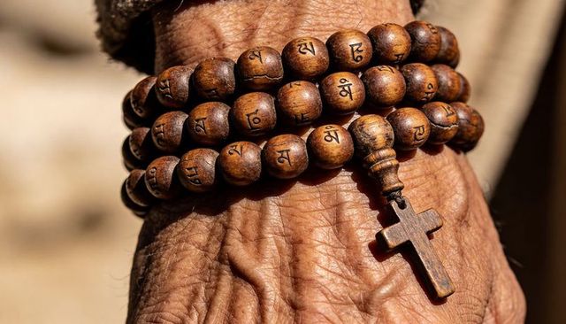 Wearing wooden prayer beads and cross on wrinkled wrist conveying quiet devotion