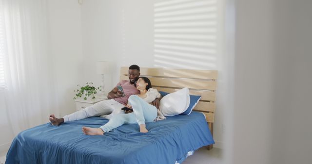 Happy diverse couple using smartphone and lying in bedroom - Download Free Stock Photos Pikwizard.com