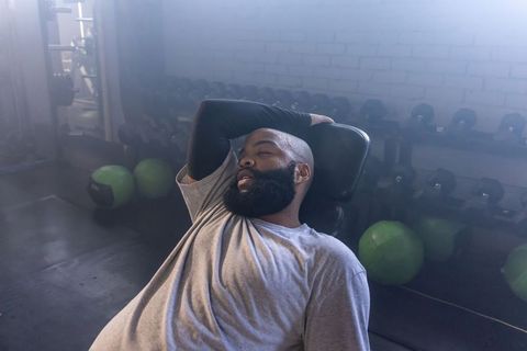 African american man resting on gym bench after workout with dumbbells in fitness studio
