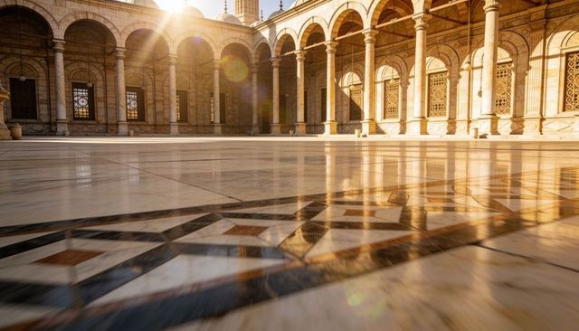 Sunlit marble courtyard reflecting warm light with geometric tile inlay and mosque arches