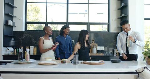 Diverse friends laughing and pouring drinks at modern kitchen island social gathering