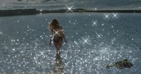 Wading toward horizon woman walking in dark bikini into sparkling shallow coastal water