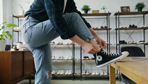 Customer tying black high-top canvas sneaker on wooden table in boutique shoe store