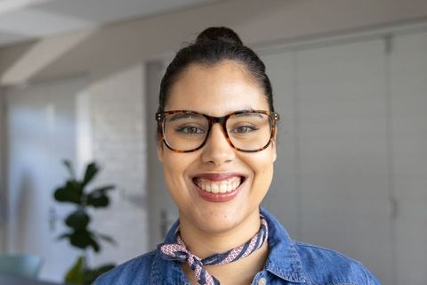 Smiling woman wearing tortoiseshell glasses and neck scarf in modern home interior