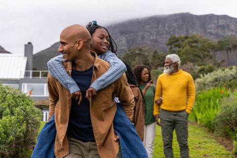 African american multigenerational family walking by coastal home, father carrying daughter