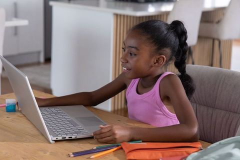African american teen studying on laptop at kitchen table, remote learning focused