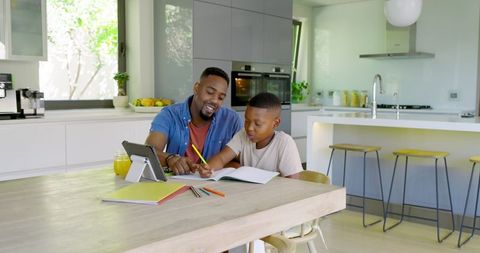 Father guiding son with schoolwork at kitchen table in bright home