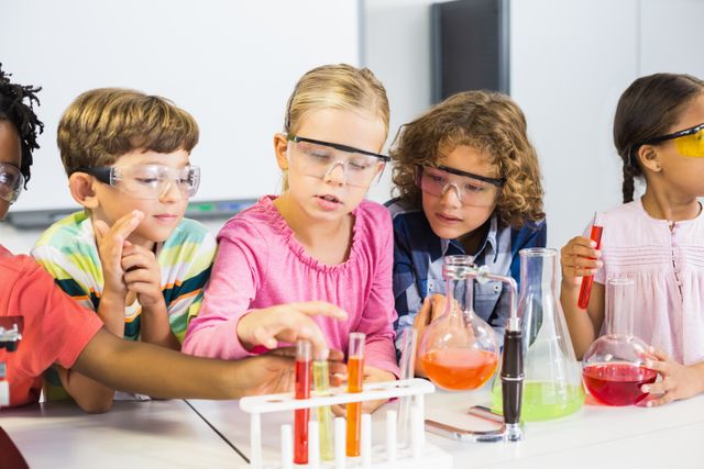 Young children are gathered around a lab table, wearing safety goggles and conducting a chemical experiment. They are using test tubes and flasks with colorful liquids, showing engagement and curiosity. Ideal for educational materials, science programs, and promoting STEM learning among children.