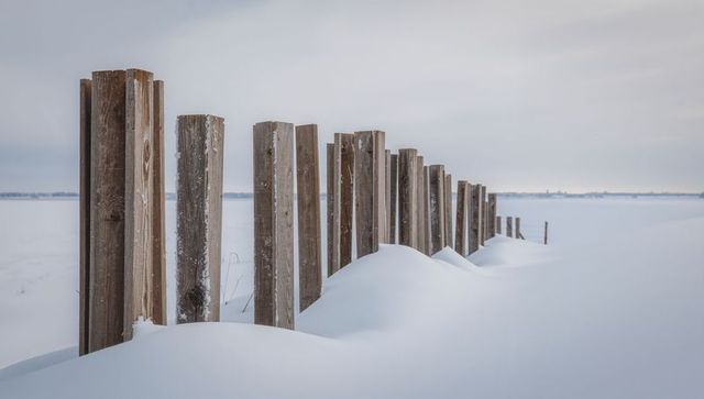 Weathered wooden posts receding through pristine snow drifts toward distant horizon