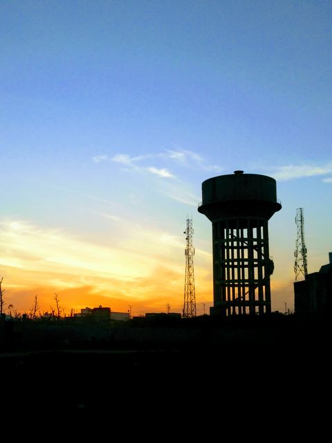 Silhouette of a watertower and communication towers against a vibrant sunset sky. Ideal for urban landscape, infrastructure themes, and telecommunications industry. Perfect for backgrounds, presentations, and promotional materials.
