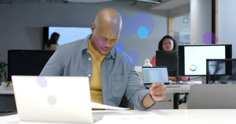 Bald Professional Reviewing Documents and Working on Laptop in Modern Open Office