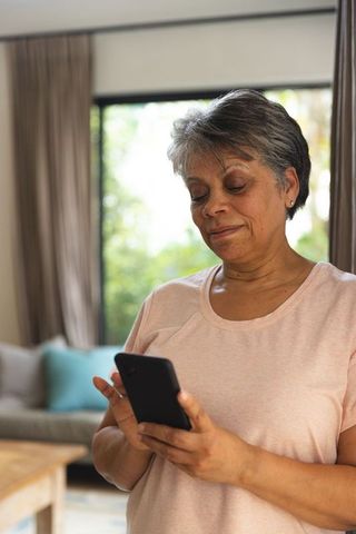 Senior woman using smartphone by living room window