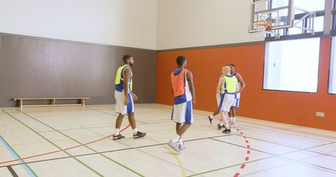 Basketball team practicing on indoor court with uniforms and pinnies