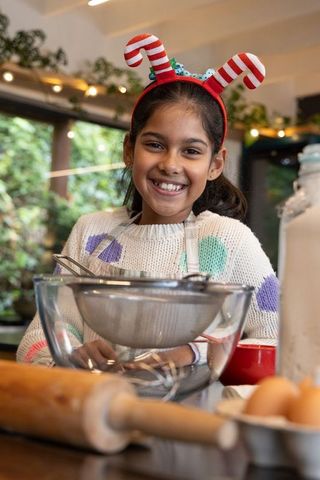 Joyful indian girl wearing candy cane headband baking at kitchen counter holiday moment