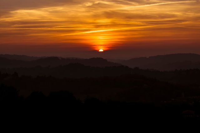 Beautiful sunset casting a warm orange glow over rolling hills and a silhouetted landscape. Perfect for use in travel brochures, nature magazines, and outdoor adventure blogs. Ideal for promoting serenity and natural beauty.