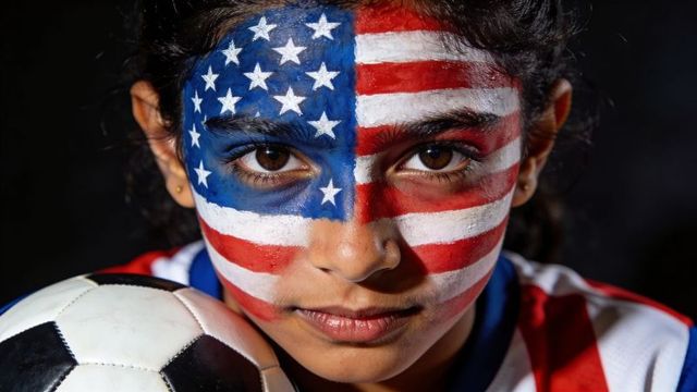 Youth soccer fan wearing full-face american flag paint holding ball closeup portrait
