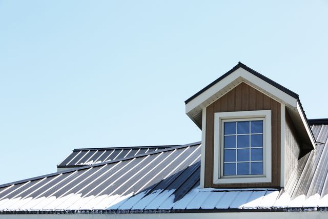 Metal roof barn featuring dormer window captures modern rural architecture with partial snow coating. Use for construction materials, winter building maintenance, rural living concepts, or farm building design ideas.