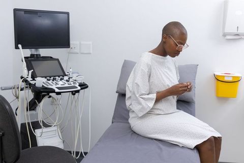 African female patient sitting on exam couch checking object near ultrasound machine