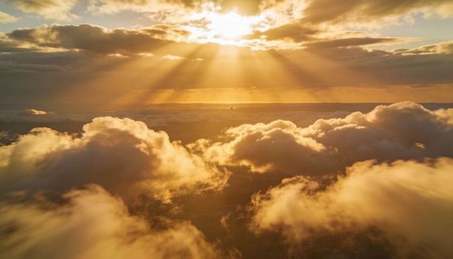 Golden sunbeams breaking through cumulus sea over distant horizon at golden hour