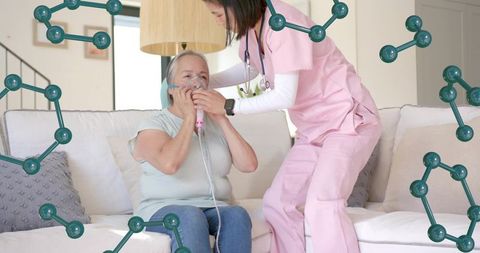 Nurse assisting senior woman with nebulizer treatment on sofa at home