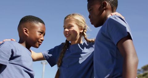 Multiracial kids huddling outdoors wearing matching blue shirts smiling showing teamwork