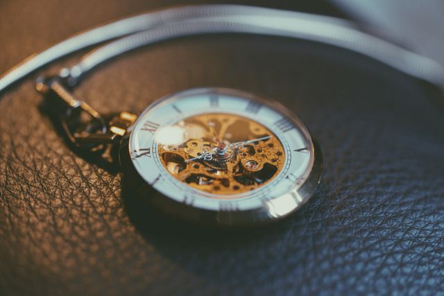 This image showcases a vintage pocket watch with exposed mechanical gears, resting on a textured leather surface. Ideal for use in topics related to timekeeping, vintage collectibles, horology, or antique jewelry. It conveys themes of elegance, craftsmanship, and timeless style.