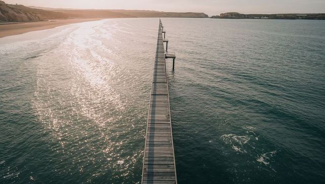 Stretching wooden pier leading to horizon with golden sun reflecting on ocean