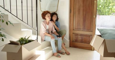 African American women sitting on stair landing unpacking moving boxes and holding phone