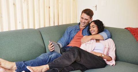 Diverse Couple Relaxing on Sofa Browsing Tablet at Home