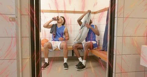 Basketball players cooling down in locker room drinking water changing jerseys using towels