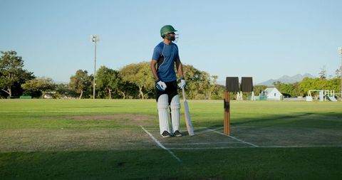 Cricketer standing at crease in green helmet and pads holding bat on sunlit cricket field