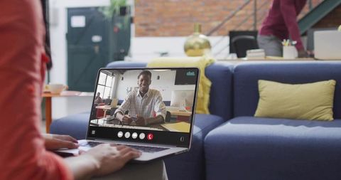 Remote team collaborating over laptop video call in modern coworking lounge with blue sofa