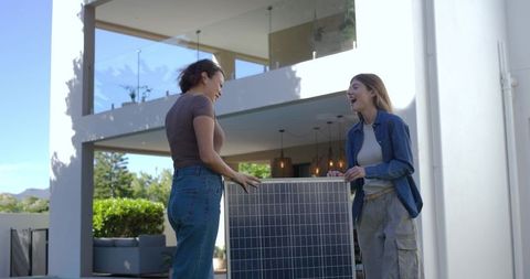 Women holding solar panel on home patio discussing sustainable energy project for home retrofit