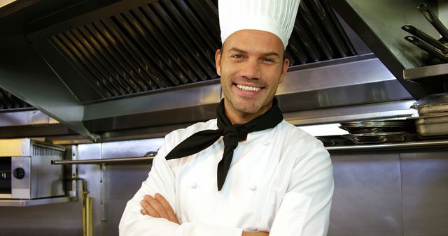 Male chef standing confidently in a modern industrial kitchen with arms crossed and black neckerchief. Ideal for promoting culinary schools, restaurant businesses, and food-related services. Highlighting professionalism, skill, and the inviting atmosphere of a well-run kitchen.